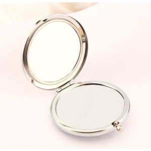 A round, double-sided makeup mirror with a shiny silver finish, opened to display both reflective surfaces.