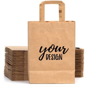 A kraft paper gift bag with handles, featuring a placeholder design on the front, set against a stack of similar bags.