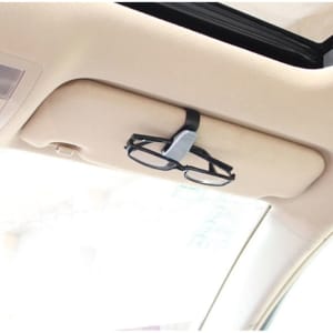 A black car glasses clip mounted on a vehicle's overhead visor, holding a pair of glasses.