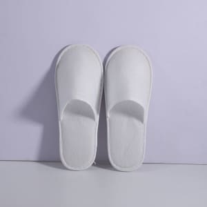 White anti-slip cloth hotel slippers displayed against a light purple background. The slippers have an open-toe design.