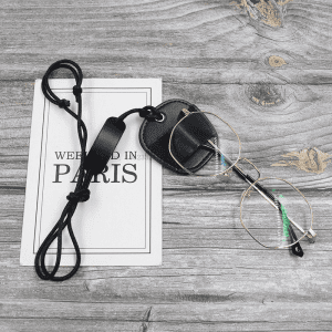 A black leather glasses neck holder with a strap and a pair of silver glasses, resting on a wooden surface.