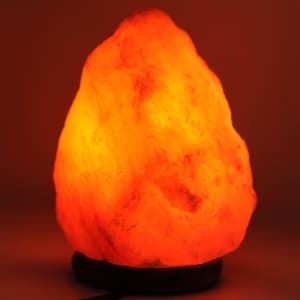 A Himalayan salt lamp in an irregular rock shape, glowing warm orange against a dark background. It has a wooden base.
