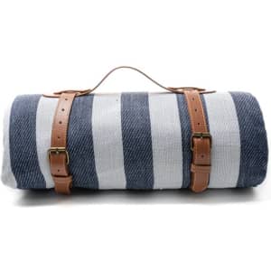 A striped picnic blanket in navy and white, featuring leather carry handles and buckles for easy transport.