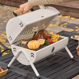 A portable drum barbecue charcoal grill in white, featuring grilled vegetables and herbs inside.