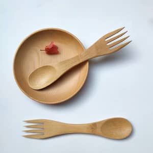 A bamboo spoon and fork set in a wooden plate, featuring a natural finish and a small decorative item.