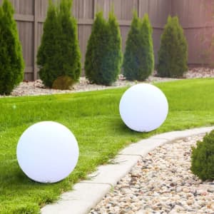 Two white luminous balloons are placed on a grassy area, surrounded by neatly trimmed hedges and gravel pathways.