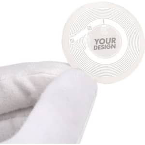 A hand holds a round, transparent NFC tag sticker featuring a circular design and space for custom artwork.