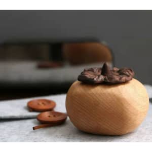 Persimmon-shaped aroma diffuser in natural wood with a brown top. Includes wooden buttons nearby.