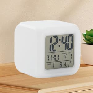 A white cube-shaped alarm clock with a digital display showing the time, date, and temperature.