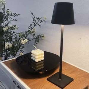 A black LED table lamp stands on a wooden surface beside a round black plate and a decorative candle.