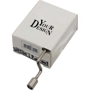 A hand crank music box in a white and black box, featuring a metal crank handle. The box has a branding logo.