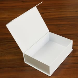 A white flip top magnetic gift box is open, displaying its empty interior against a wooden surface.