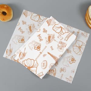 Custom wrapping paper featuring brown illustrations of desserts and flowers on a white background, with some baked goods nearby.