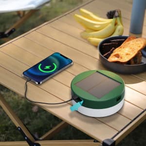 A green and white solar camping string light on a wooden table, with a smartphone and food items nearby.