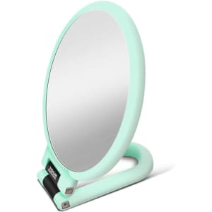 A mint green handheld magnifying makeup mirror with a sturdy stand. Features a logo at the base.
