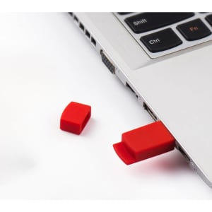 A red silicone USB flash drive partially inserted into a laptop with a matching cap alongside it.