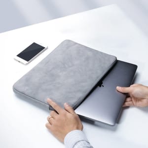 A grey custom laptop sleeve is being used to hold a laptop. A smartphone is visible in the background.