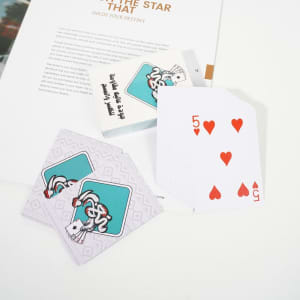 Custom PVC playing cards featuring a colourful design, with a red five of hearts displayed and a branded box.