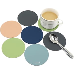 A coffee cup on a green silicone coaster surrounded by six coloured coasters in peach, navy, green, blue, and grey.