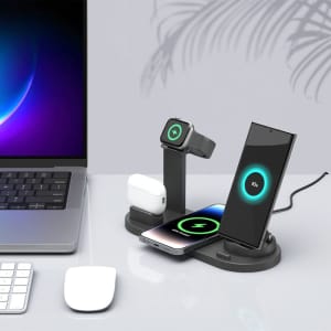 A black 4-in-1 wireless charging stand with compartments for a smartphone, AirPods, and a smartwatch on a desk.