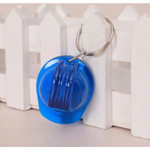 A blue plastic safety helmet keychain attached to a silver metal ring, set against a white picket fence background.