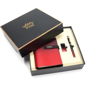 A red notebook, pen, and clip presented in a sleek black gift box with gold accents and a logo.