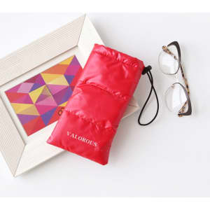 A red puffer drawstring bag beside a pair of glasses and an artwork in a frame. The bag has a logo.