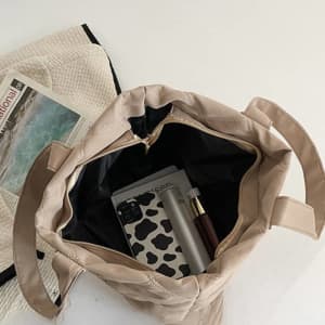 A large beige tote handbag with a black interior, containing a drink bottle, phone, and other items.