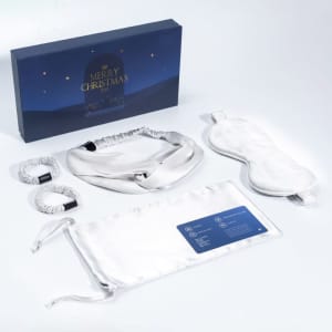 A silk eye mask gift set in silver, including an eye mask, headband, and two scrunchies, presented in a festive box.