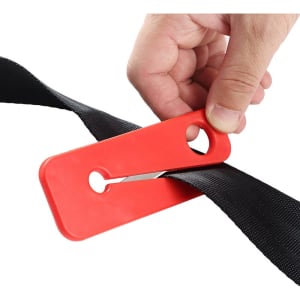 A red plastic safety belt cutter being used to slice through a black strap. The tool features a hole for attachment.