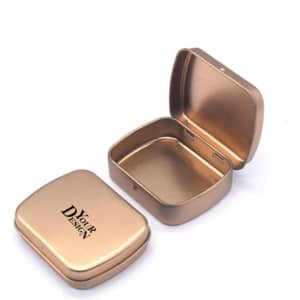 A gold metal hinged box container with a smooth interior and a logo printed on the lid.