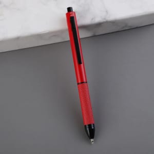 A red 4-in-1 ballpoint pen with a textured grip and a black clip, placed on a grey surface.