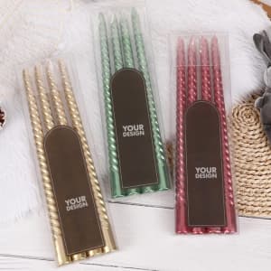 A set of four spiral taper candles in gold, green, and red, packaged in a clear box with a logo.