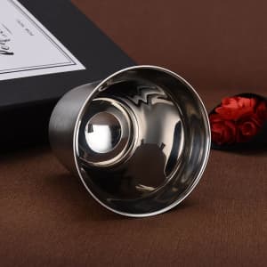 A stainless steel coffee mug with a polished interior, presented in a boxed setting alongside red flowers.