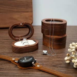 A wooden portable jewelry box with a ring inside, accompanied by necklaces and a watch on a wooden surface.