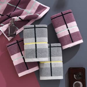 Four custom cotton towels in shades of grey, pink, and purple, featuring striped patterns, stacked together on a surface.