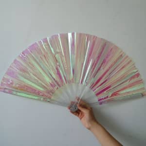 A hand holding a large, pink and iridescent PVC folding fan with a transparent handle.