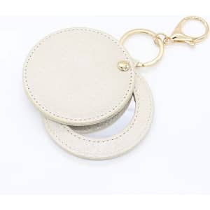 A beige compact mirror with a keychain, featuring a smooth surface and a gold-tone clip.