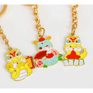 Three gold keychains featuring colourful designs of cute dragon characters, adorned with festive details.