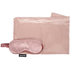 A satin pillowcase and matching sleep mask in soft pink, featuring a logo and a smooth finish.