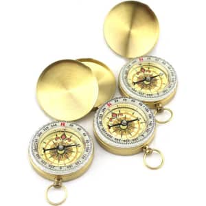 A set of three brass compasses with a clear face, featuring directional markings and a protective lid.