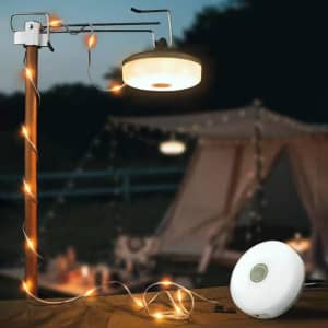 A portable camping string light with a white circular design, suspended from a pole, illuminating a campsite setting.