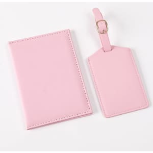A pink passport holder and matching luggage tag, made from soft material, featuring a simple design and a logo.
