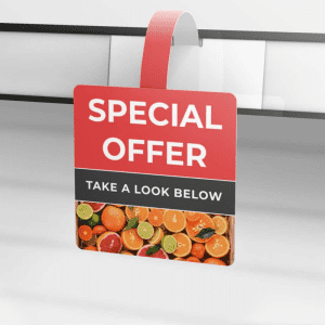 A red and black shelf wobbler hanging from a supermarket shelf, featuring fruit imagery at the bottom.