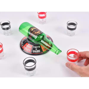 A green drink bottle resting on a game base, surrounded by clear shot glasses in red and black.