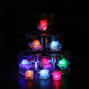 A stack of glasses contains colourful LED light-up ice cubes, glowing in red, blue, green, and yellow against a dark background.
