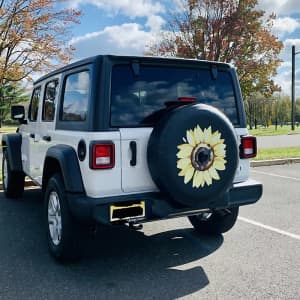 A custom spare tire cover featuring a sunflower design, fitted on a white SUV in an outdoor setting.