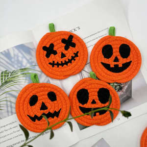 Four orange pumpkin-shaped coasters with black faces, featuring various spooky expressions and green leaves.