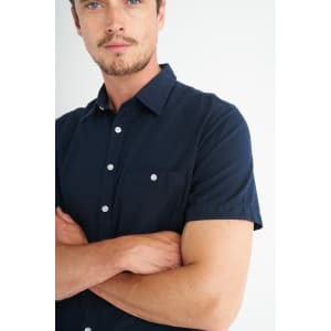 A navy blue short sleeve button-up shirt featuring a chest pocket and white buttons.