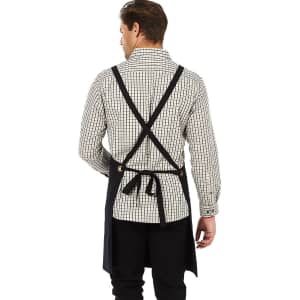 A black bib apron with crossed straps is displayed on a person wearing a checked shirt. The apron features a logo.
